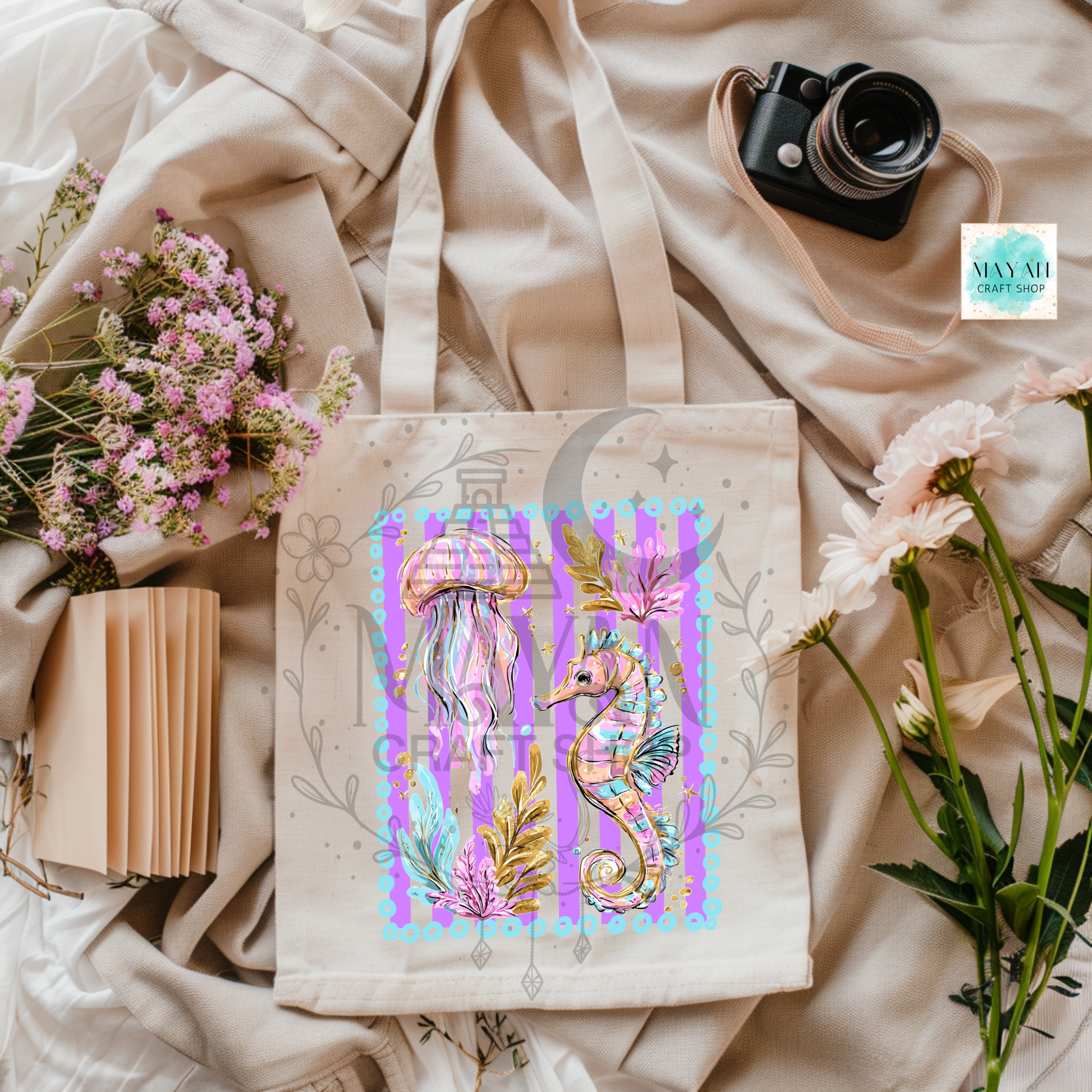 Tote bag with seahorse design on a fabric background with flowers and a camera.