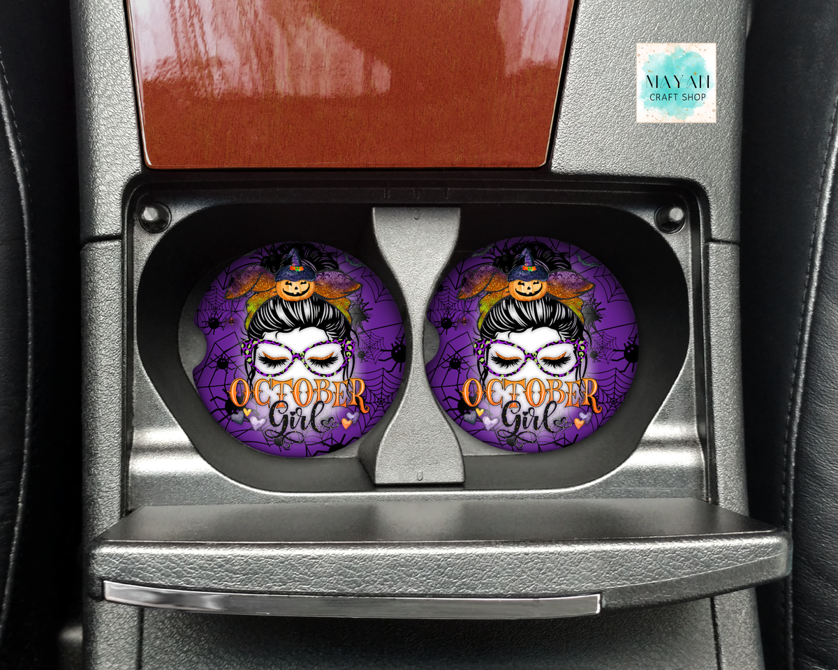 Two round car cup holders featuring a purple Halloween-themed design with a witch character and the text 'October Girl' are installed in a car center console.
