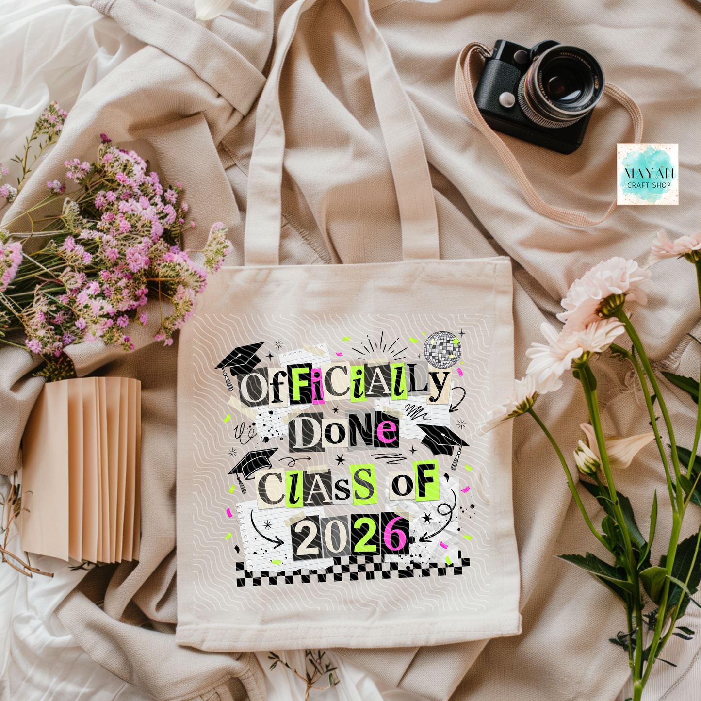 Tote bag with 'Officially Done Class of 2026' design on a light fabric background with flowers and a camera.