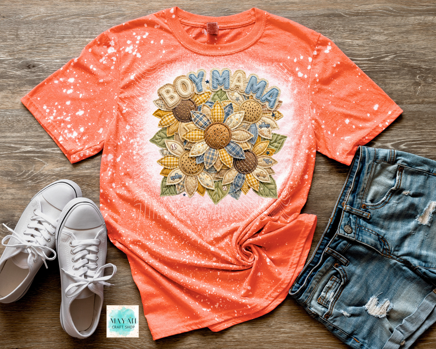 Coral t-shirt with 'BOY MAMA' and sunflower design, paired with white sneakers and denim shorts on a wooden surface.