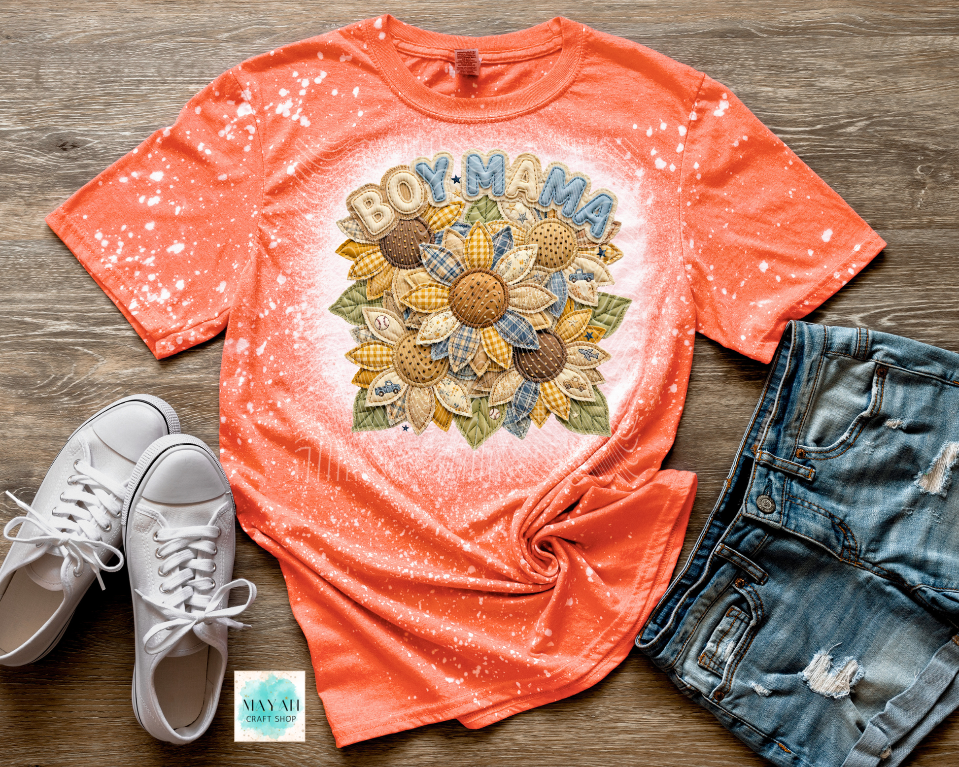 Coral t-shirt with 'BOY MAMA' and sunflower design, paired with white sneakers and denim shorts on a wooden surface.