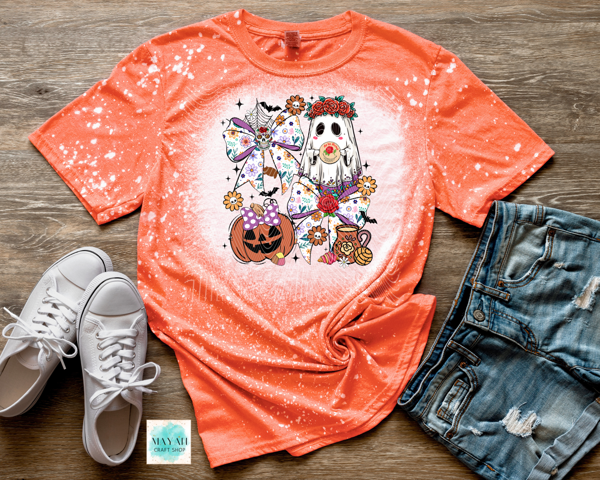 Orange t-shirt with Halloween-themed design on a wooden surface with white sneakers and denim shorts.