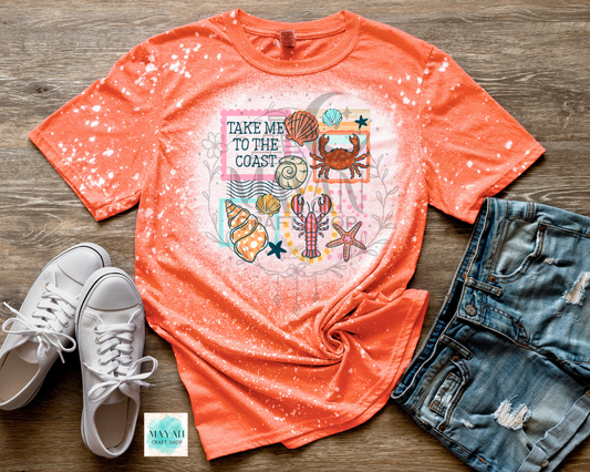 Orange t-shirt with coastal design, white sneakers, and denim shorts on a wooden surface