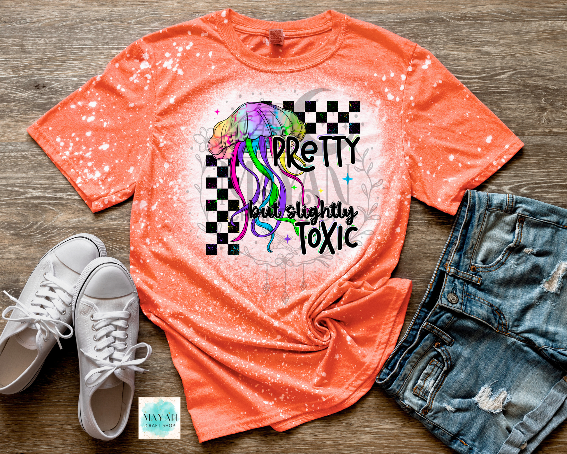 Orange t-shirt with graphic design and text, paired with white sneakers and denim shorts on a wooden surface.