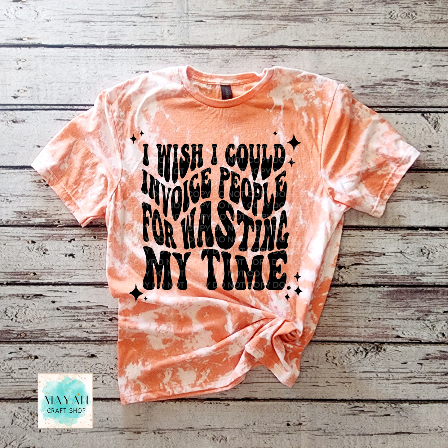 Tie-dye t-shirt with humorous text on a wooden surface, branded 'Mayan Craft Shop'.