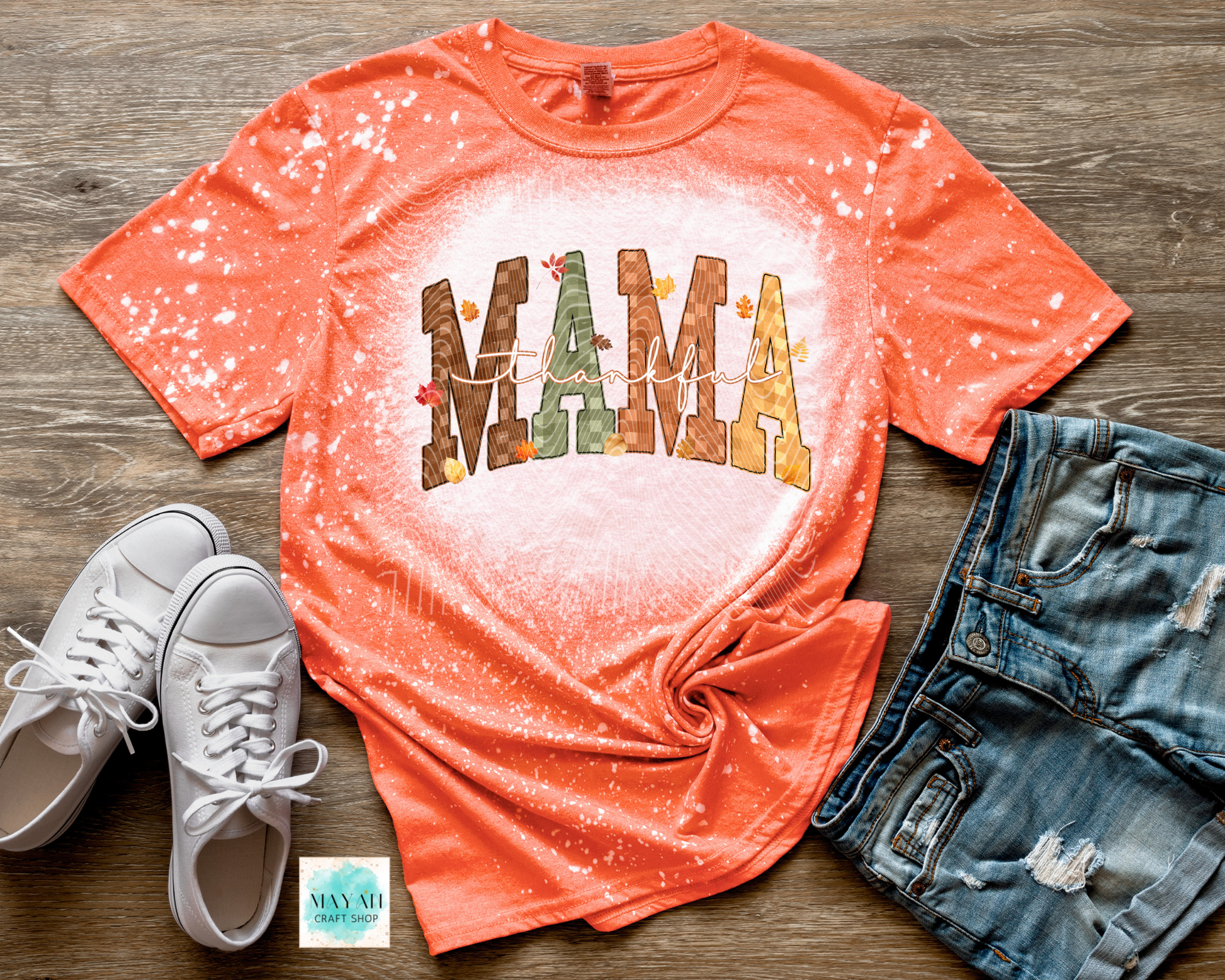 Coral t-shirt with 'MAMA' print on a wooden surface with white sneakers and denim shorts.