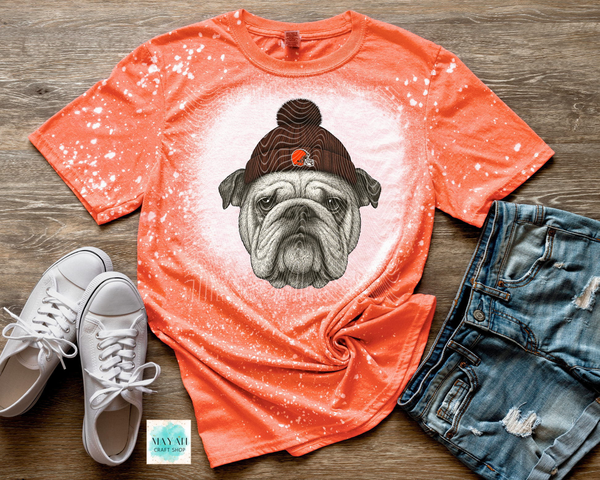 Orange t-shirt with a dog graphic, white sneakers, and denim shorts on a wooden surface.