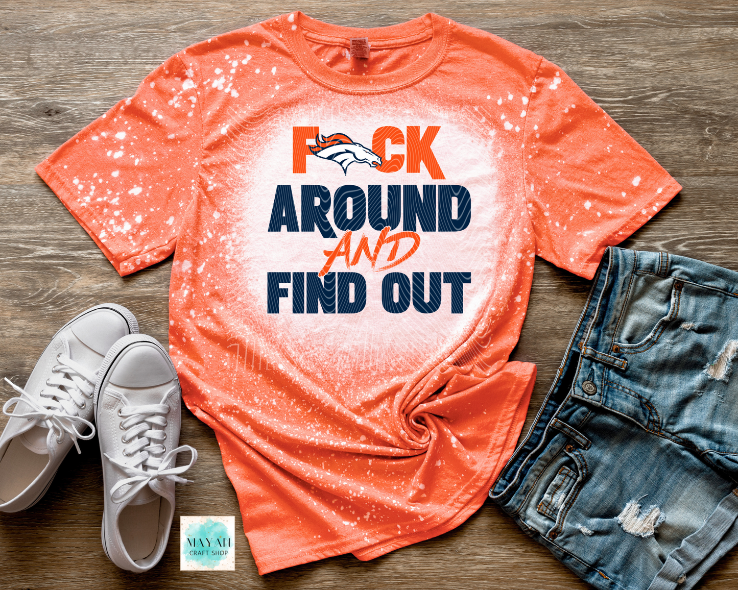 Orange t-shirt with graphic text, white sneakers, and denim shorts on a wooden surface