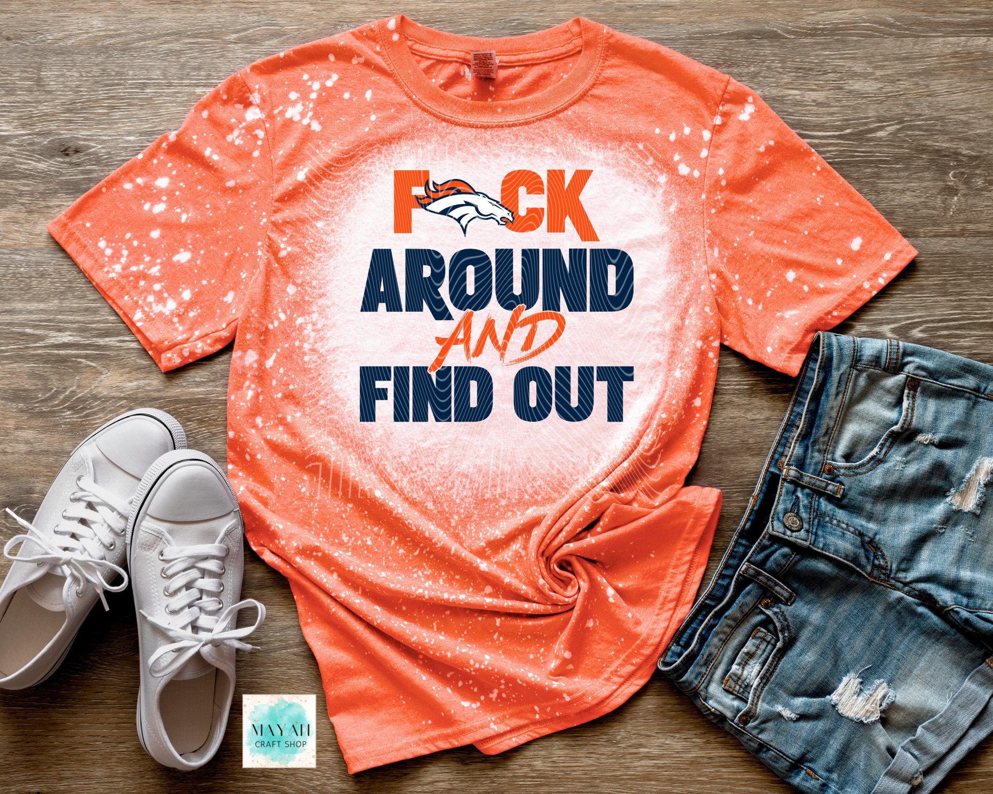 Orange t-shirt with graphic text, white sneakers, and denim shorts on a wooden surface