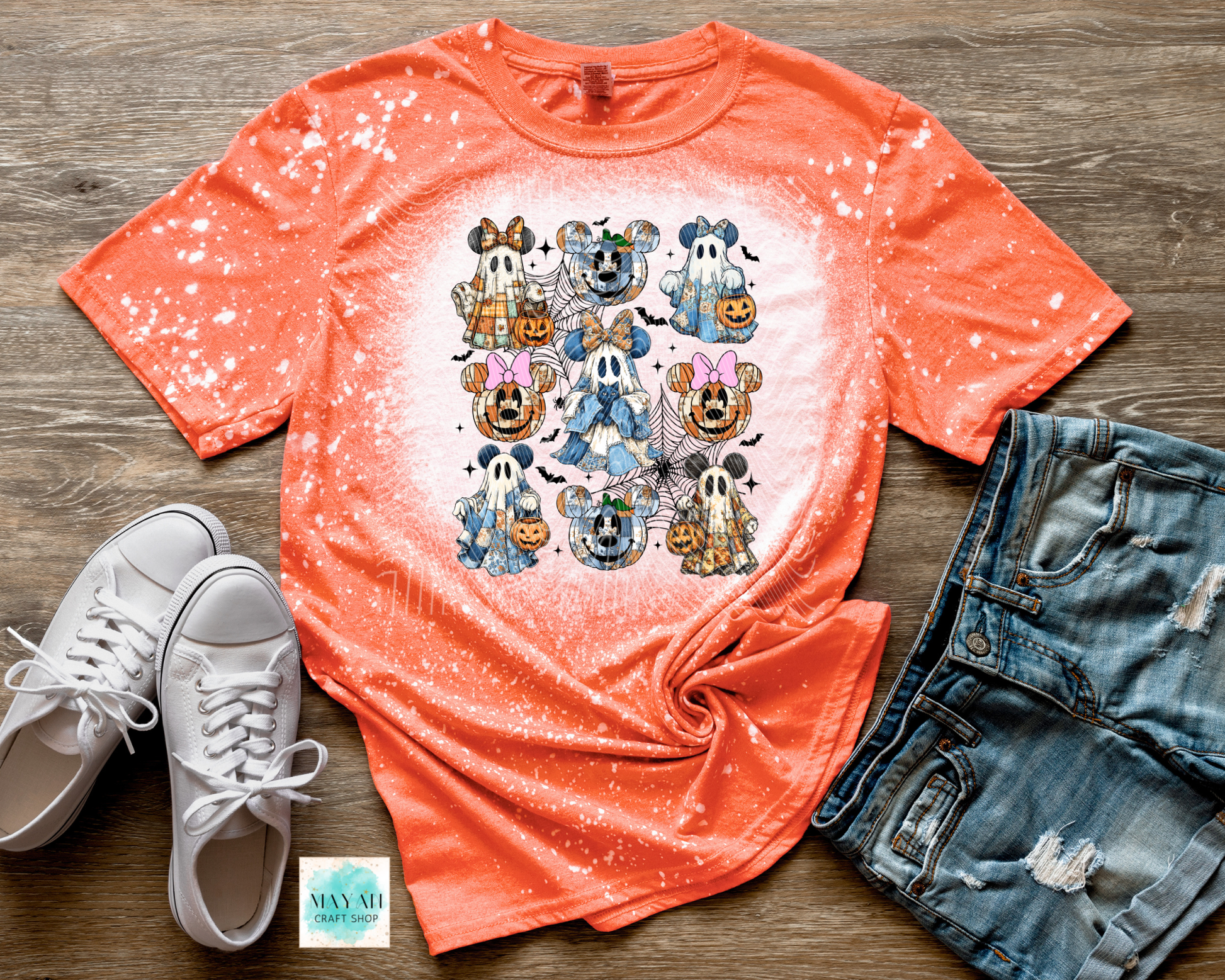 Orange t-shirt with Halloween-themed design, white sneakers, and denim shorts on a wooden surface.