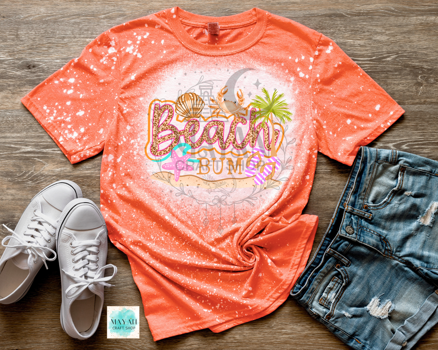 Orange t-shirt with 'Beach Bum' design on a wooden surface with white sneakers and denim shorts.