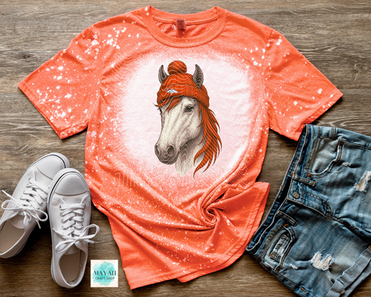 Orange t-shirt with horse graphic, white sneakers, and denim shorts on a wooden surface