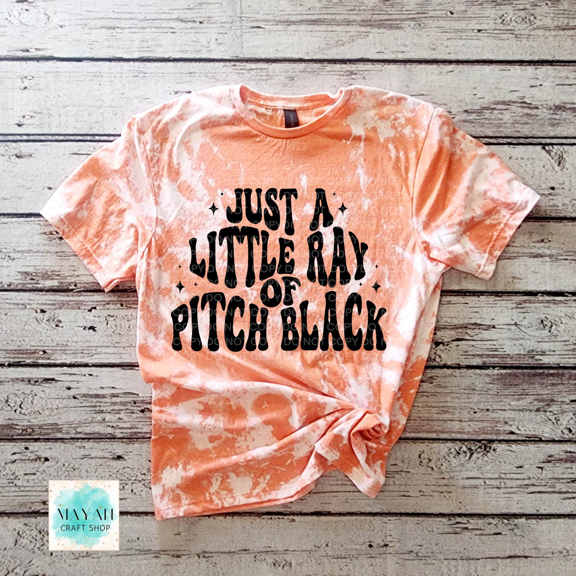 Tie-dye t-shirt with text on a wooden surface, featuring the brand 'Mayan Craft Shop'.