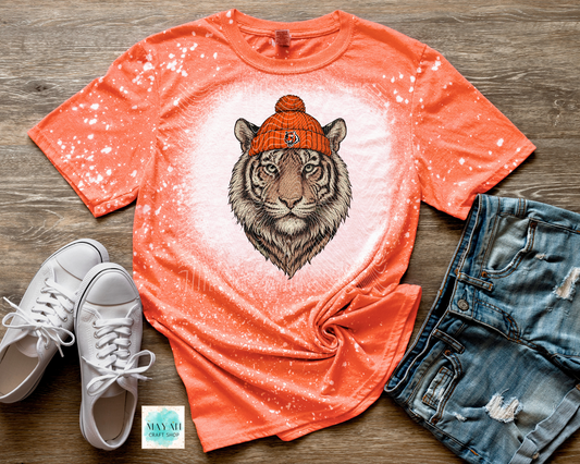 Orange t-shirt with tiger graphic, white sneakers, and denim shorts on a wooden surface