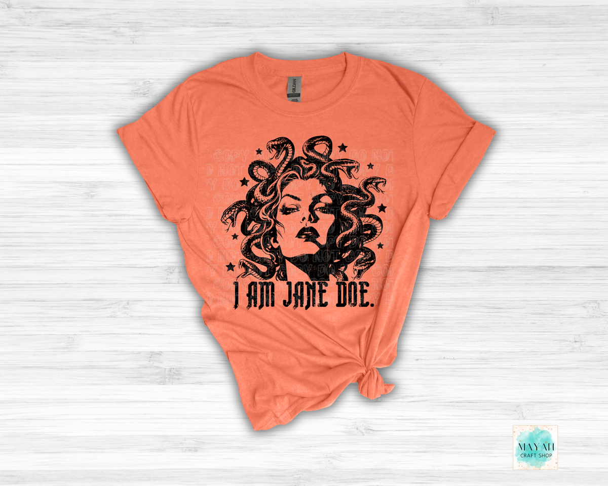 An heather orange short-sleeve t-shirt with a black graphic of Medusa's face and hair, with the text 'I AM JANE DOE.' printed below it.