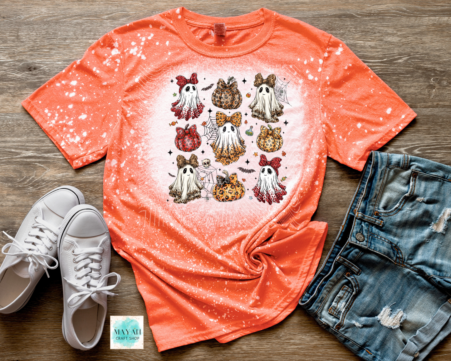 Orange t-shirt with ghost designs, white sneakers, and denim shorts on a wooden surface