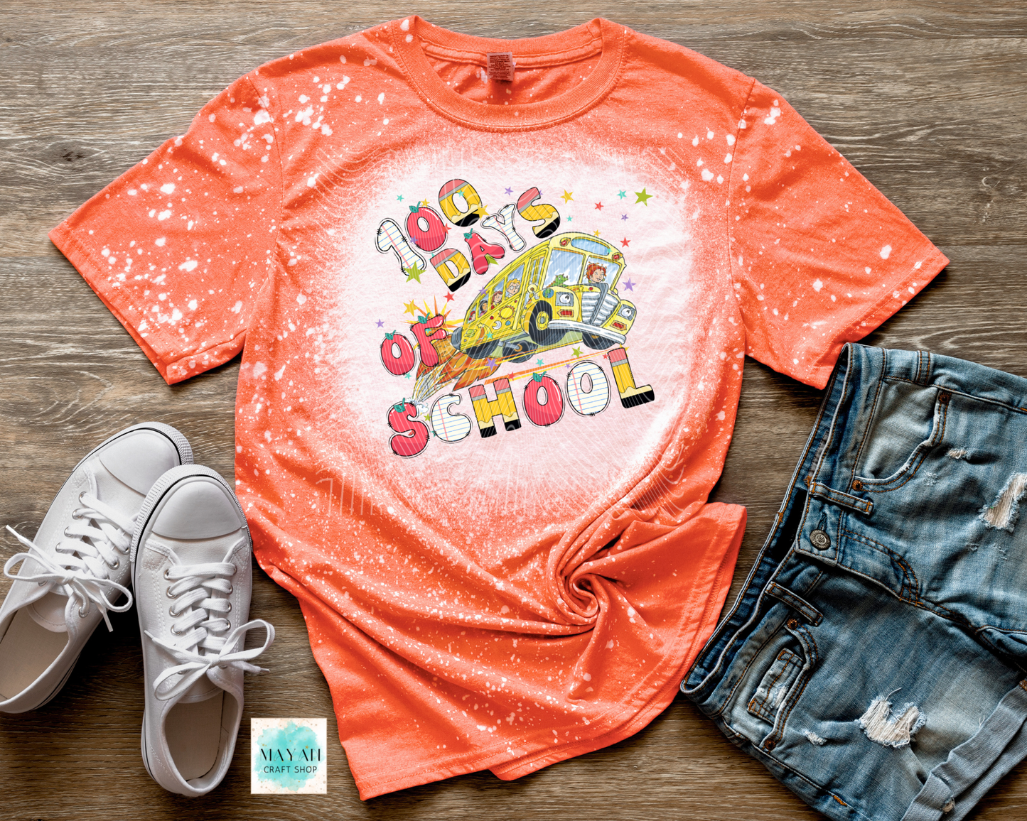 Orange t-shirt with '100 Days of School' graphic, white sneakers, and denim shorts on a wooden surface.