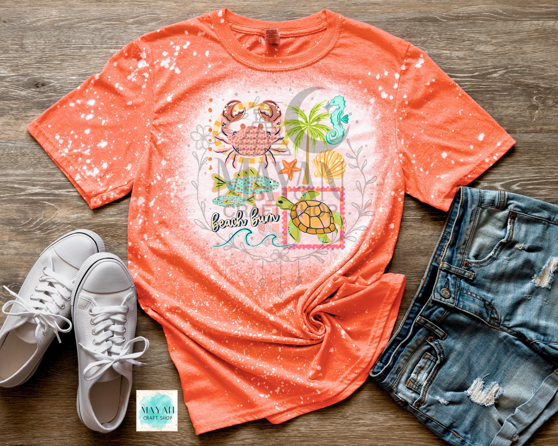 Orange t-shirt with beach-themed design, white sneakers, and denim shorts on a wooden surface.