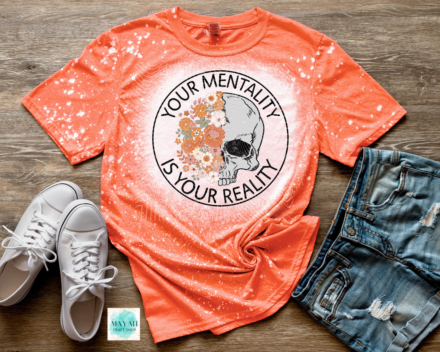 Orange t-shirt with skull and text graphic, white sneakers, and denim shorts on a wooden surface