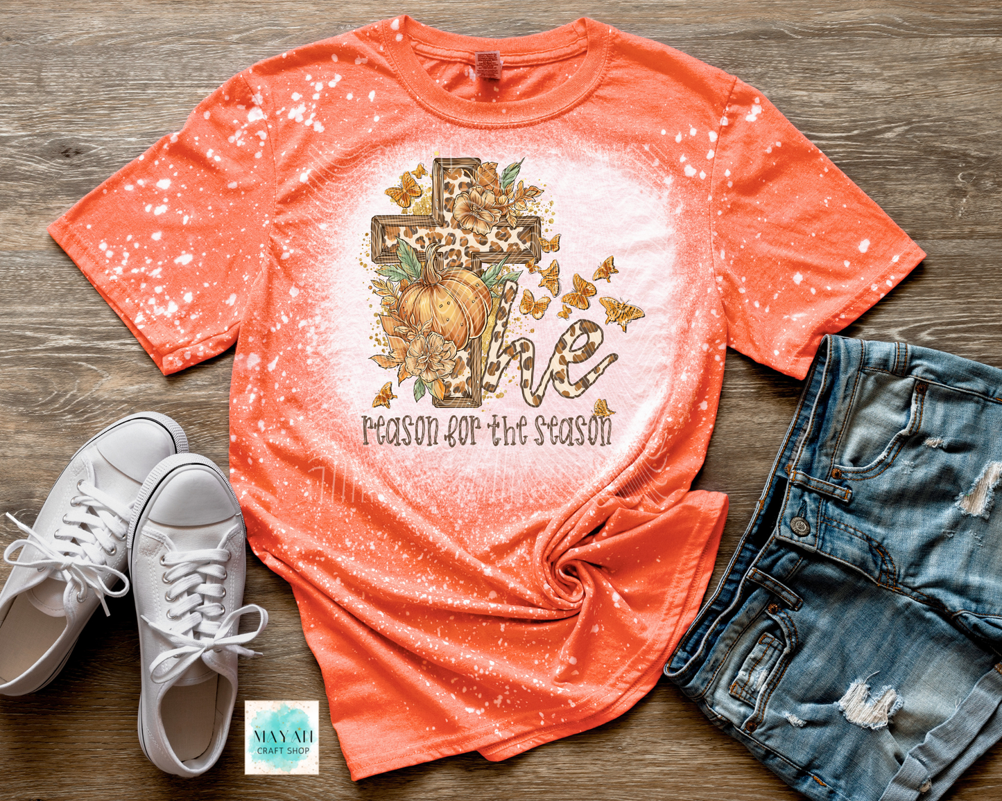 Orange t-shirt with pumpkin design and text, paired with white sneakers and denim shorts on a wooden surface.