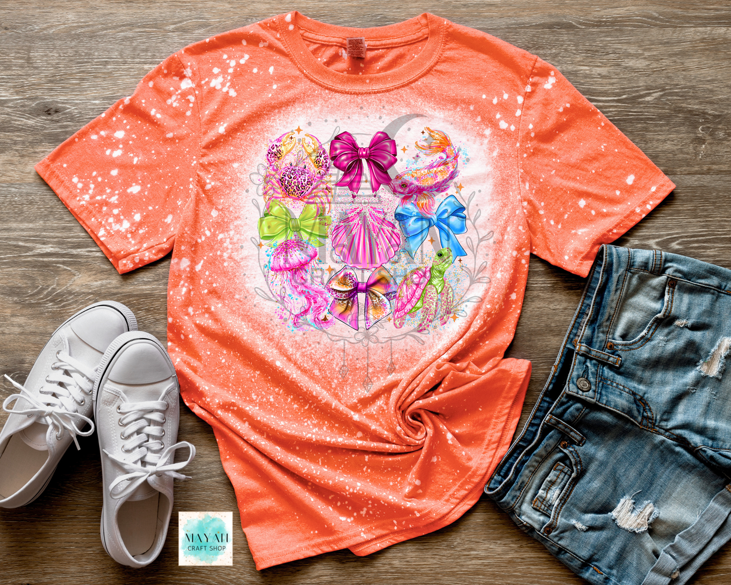 Orange t-shirt with colorful graphic design on a wooden surface with white sneakers and denim shorts.