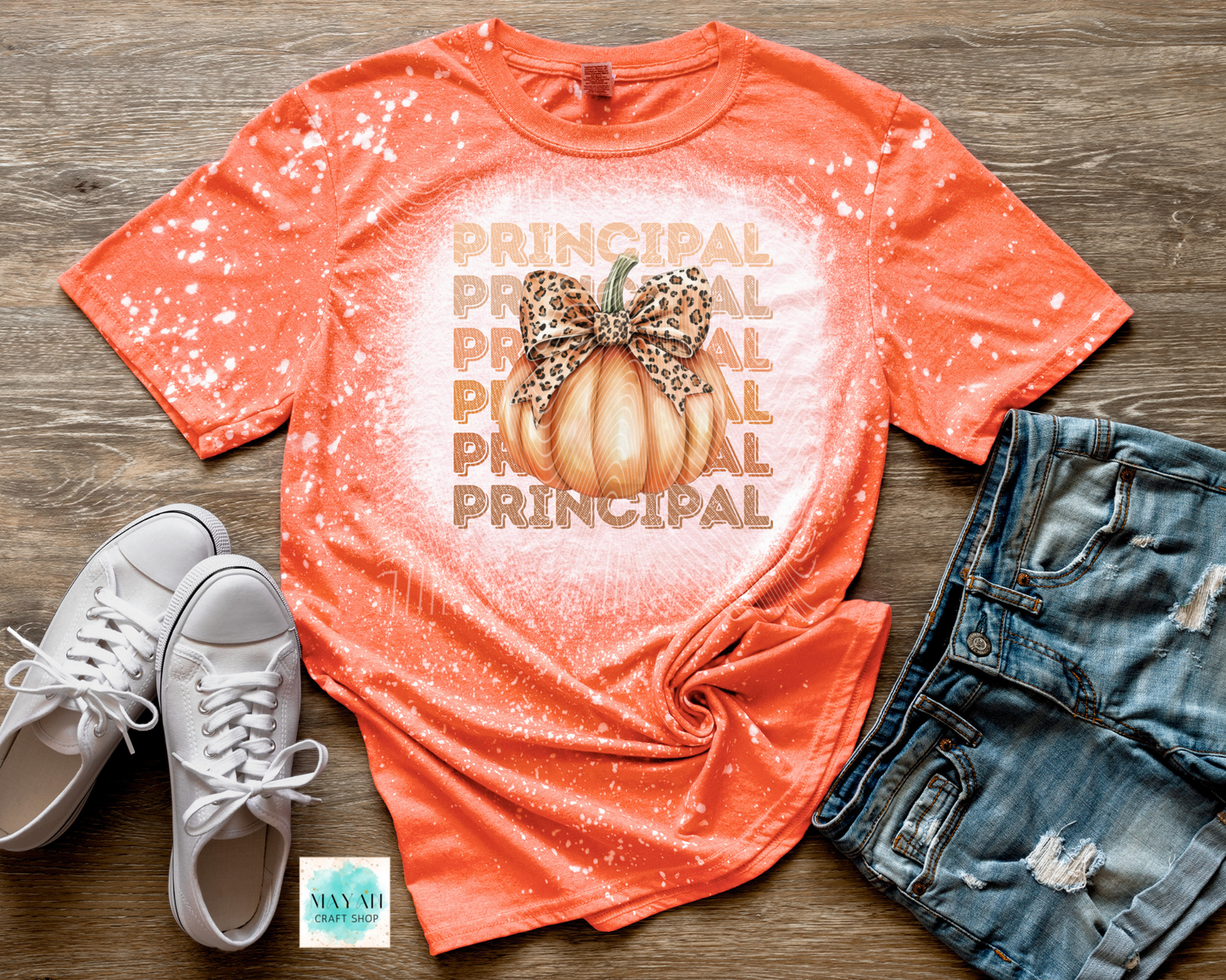 Orange t-shirt with 'Principal' and pumpkin design, paired with white sneakers and denim shorts on a wooden surface.