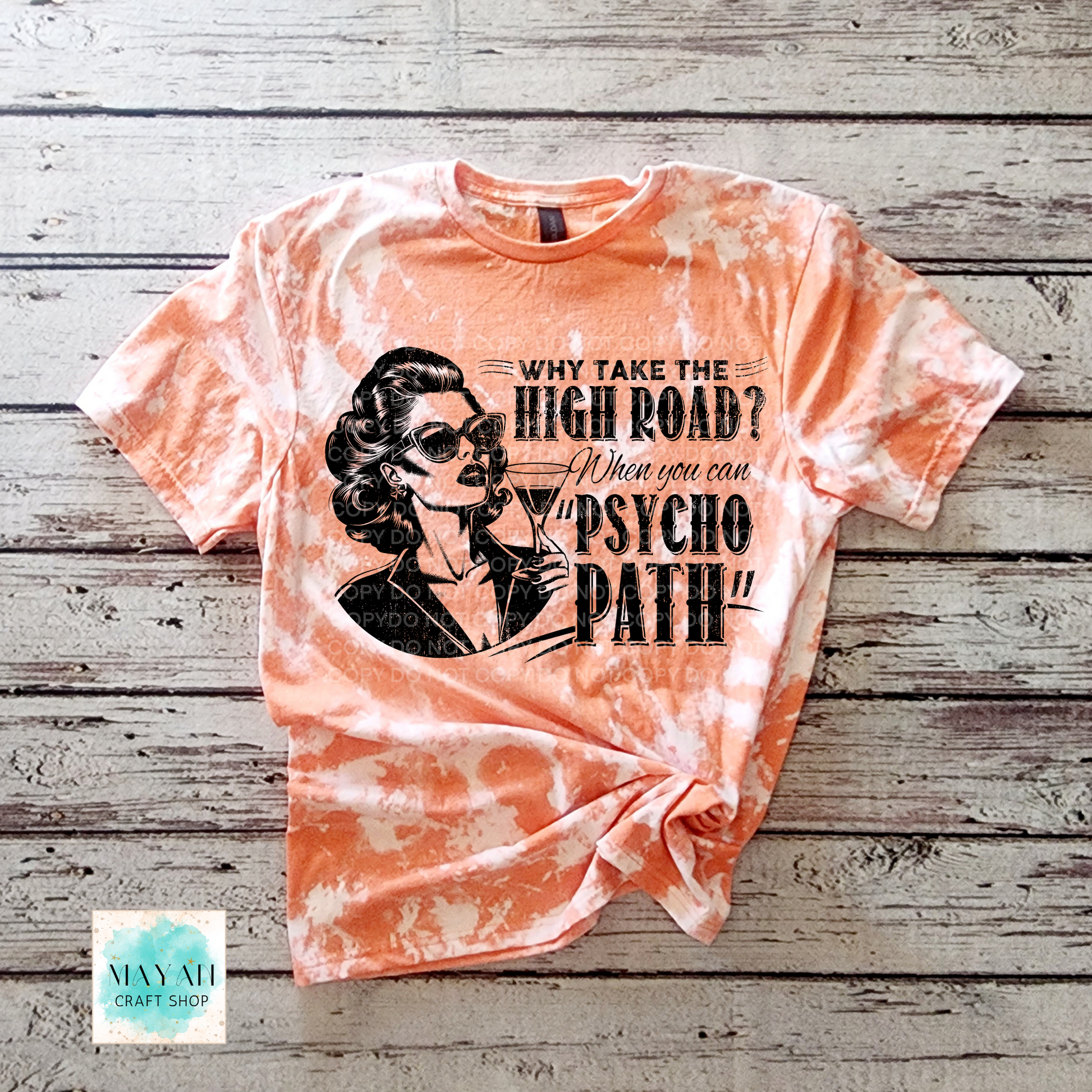 Tie-dye t-shirt with graphic design and text on a wooden surface, featuring the brand 'Mayan Craft Shop'.