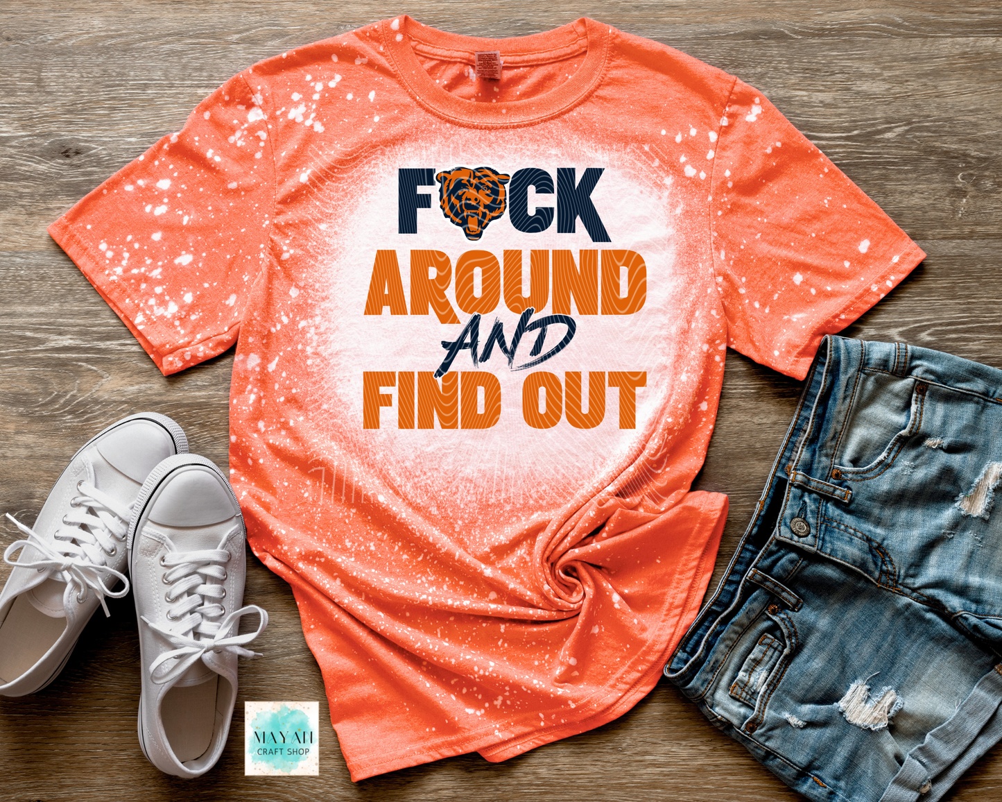 Orange t-shirt with graphic text, white sneakers, and denim shorts on a wooden surface