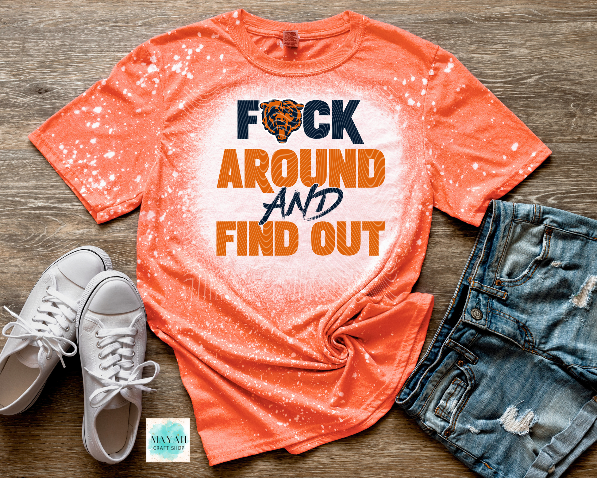 Orange t-shirt with graphic text, white sneakers, and denim shorts on a wooden surface