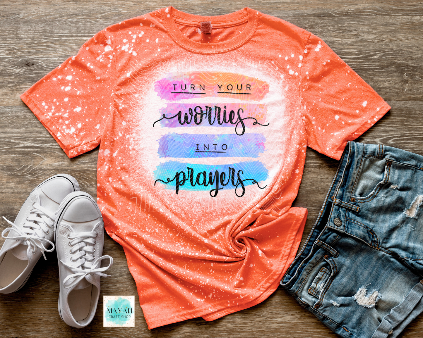 Orange t-shirt with motivational quote, white sneakers, and denim shorts on a wooden surface