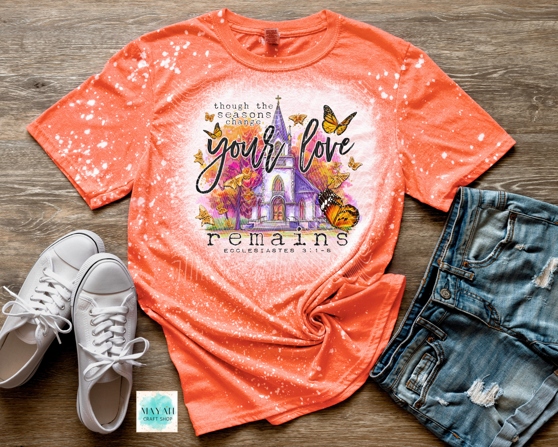 Orange t-shirt with colorful design and text on a wooden surface with shoes and shorts.
