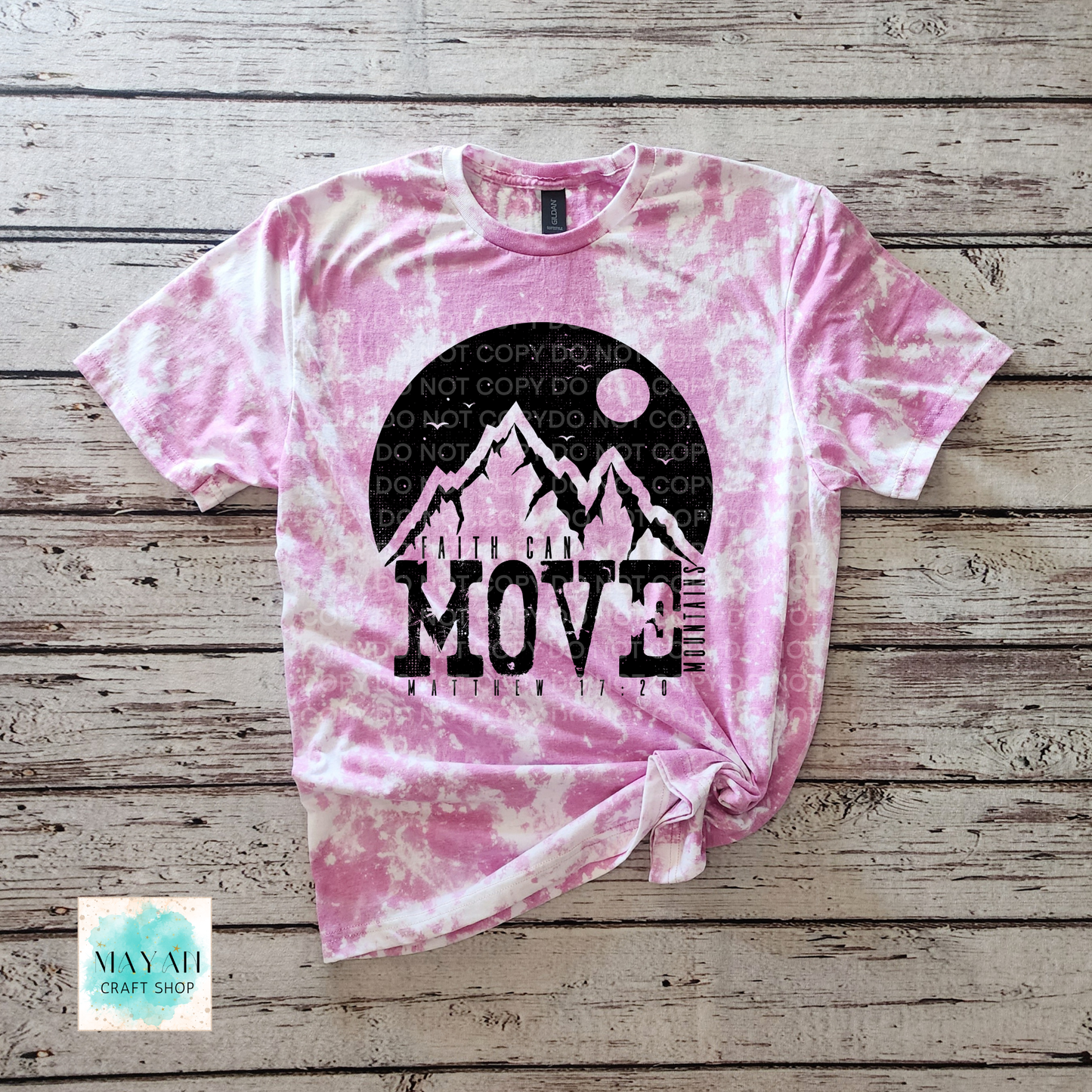 Pink tie-dye t-shirt with mountain graphic and text on a wooden surface