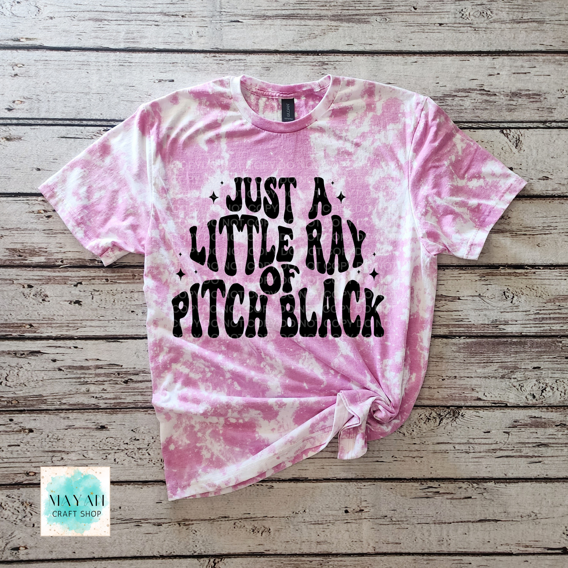 Pink tie-dye t-shirt with black text on a wooden surface, featuring the brand 'Mayan Craft Shop'.