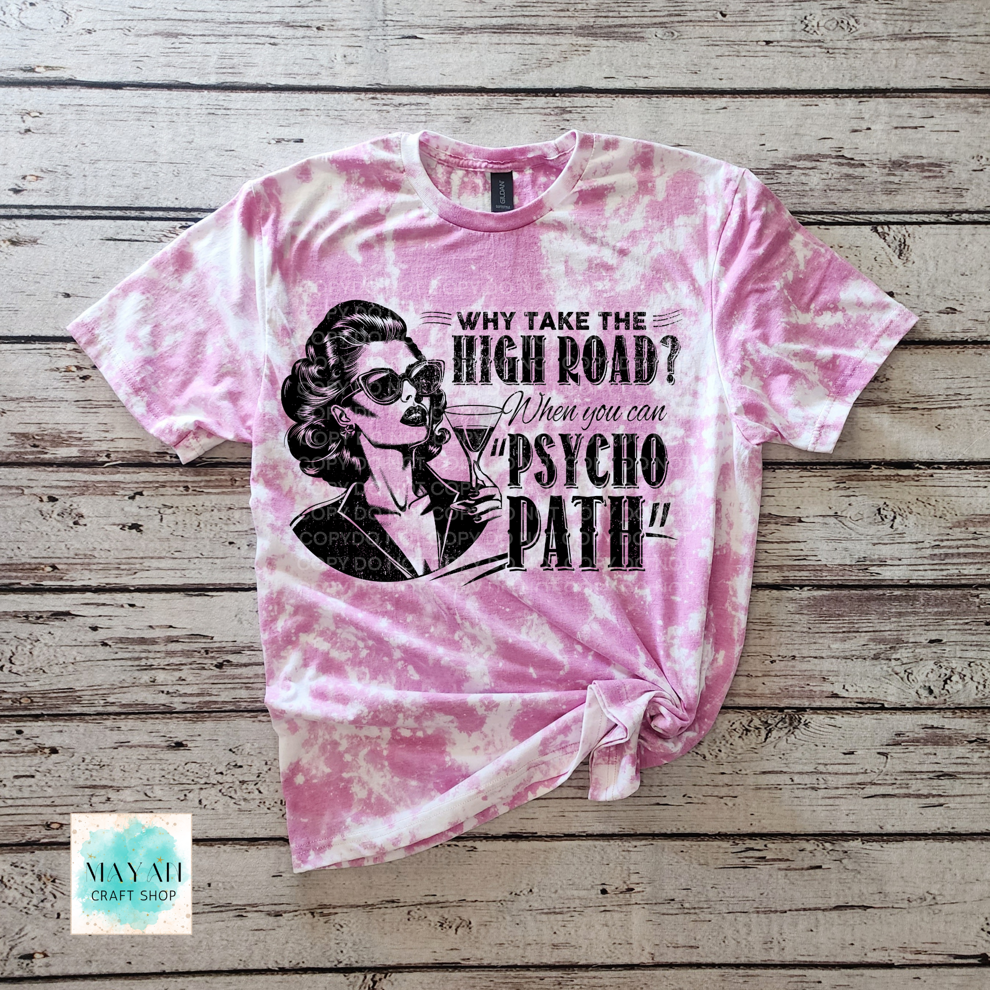 Pink tie-dye t-shirt with graphic design and text on a wooden surface, featuring the brand 'Maya Craft Shop'.