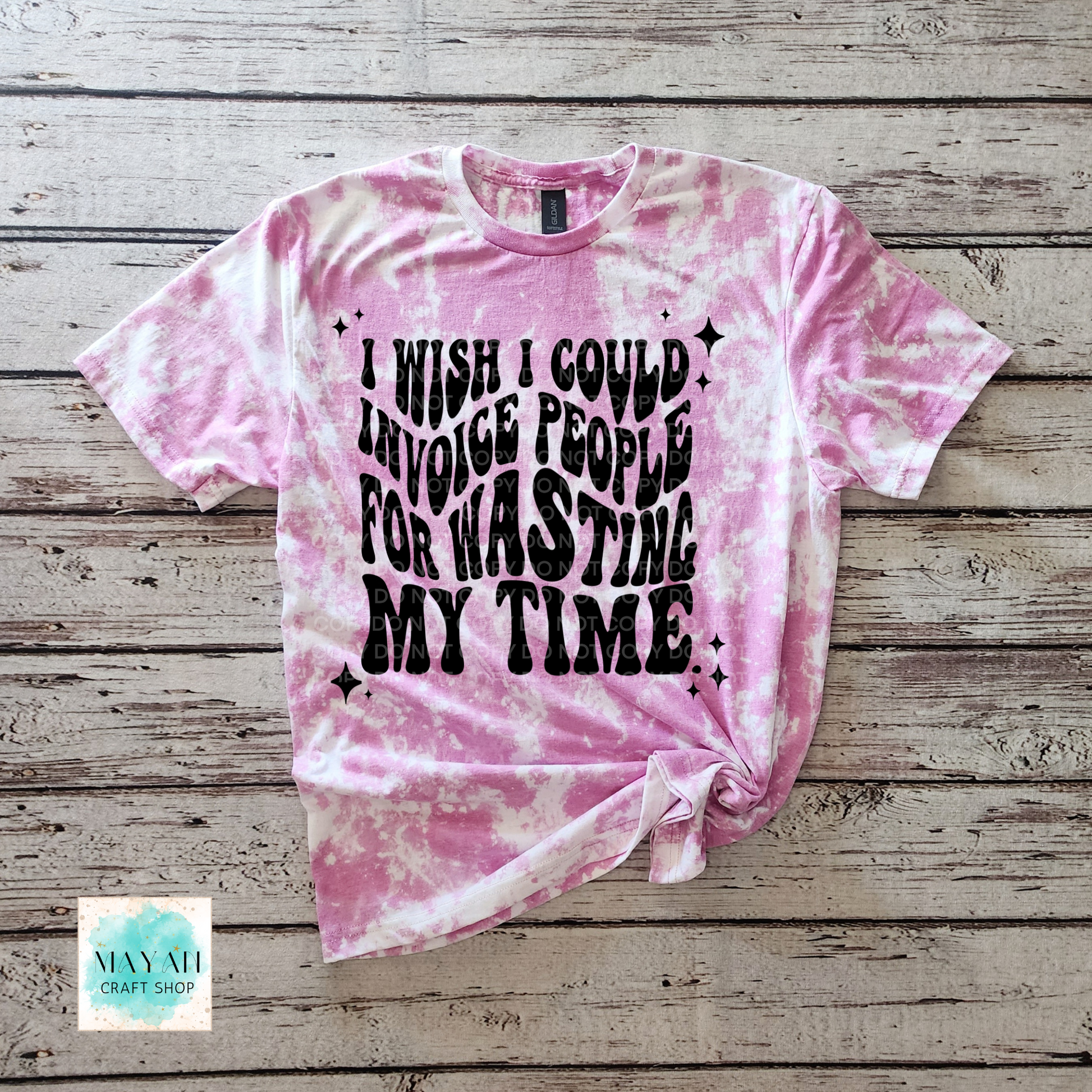 Pink tie-dye t-shirt with black text on a wooden surface, featuring the brand 'Mayan Craft Shop'.