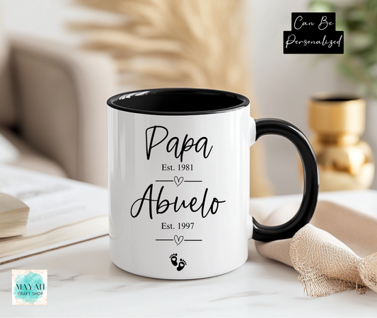 White mug with black interior and handle displaying 'Papa Est. 1981' and 'Abuelo Est. 1997' text, placed on a surface.