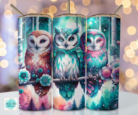 Three colorful owl tumblers with floral designs on a blurred bokeh background.
