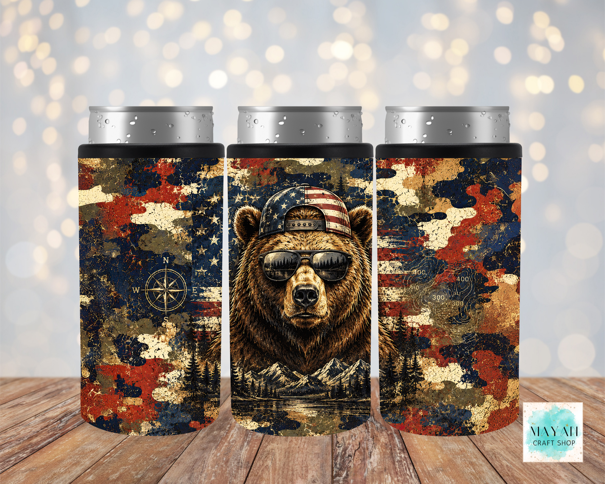 Three cylindrical can coolers with a bear design featuring an American flag and camouflage pattern on a wooden surface.