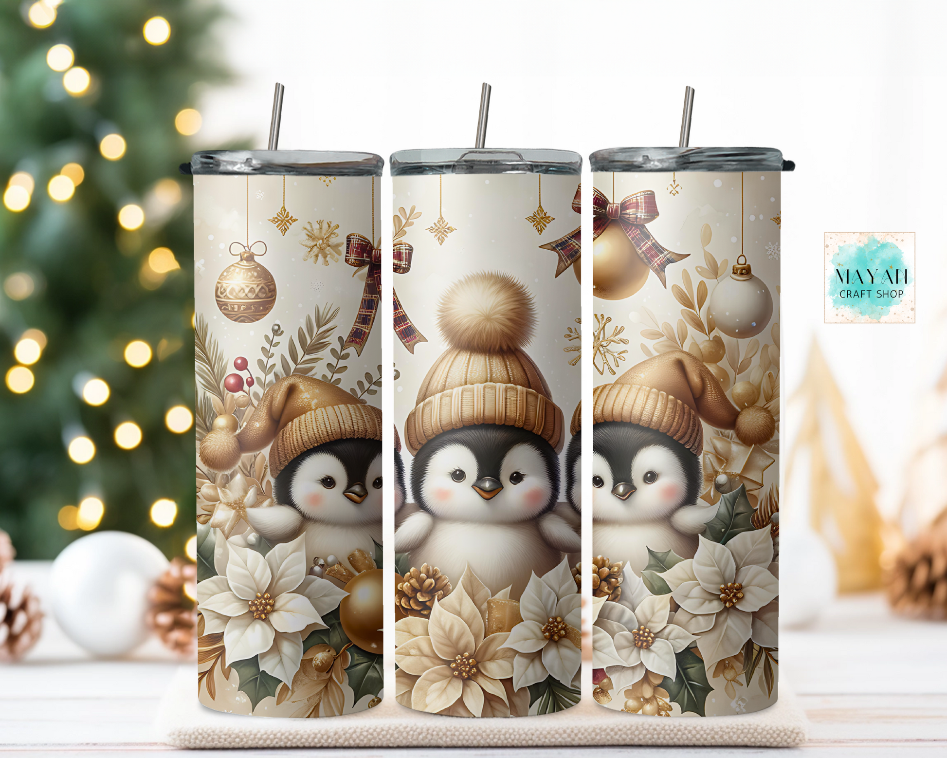 Three tumblers with penguin design and Christmas elements on a wooden surface with a blurred Christmas tree background.