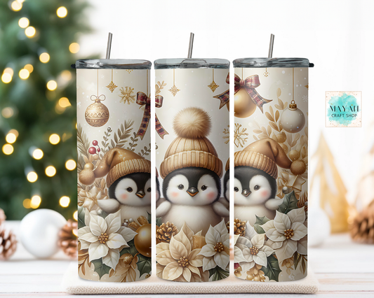Three tumblers with penguin design and Christmas elements on a wooden surface with a blurred Christmas tree background.