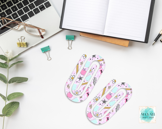 Two pink paper clips with a pattern on a desk with office supplies.