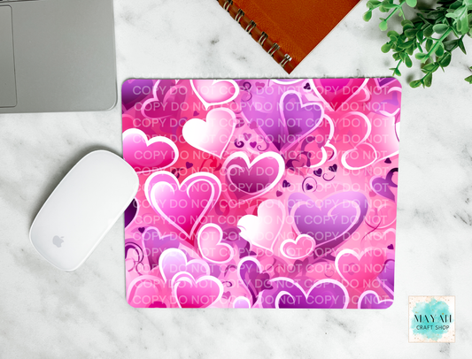 Pink and purple heart patterned mouse pad on a marble surface with a laptop and mouse.