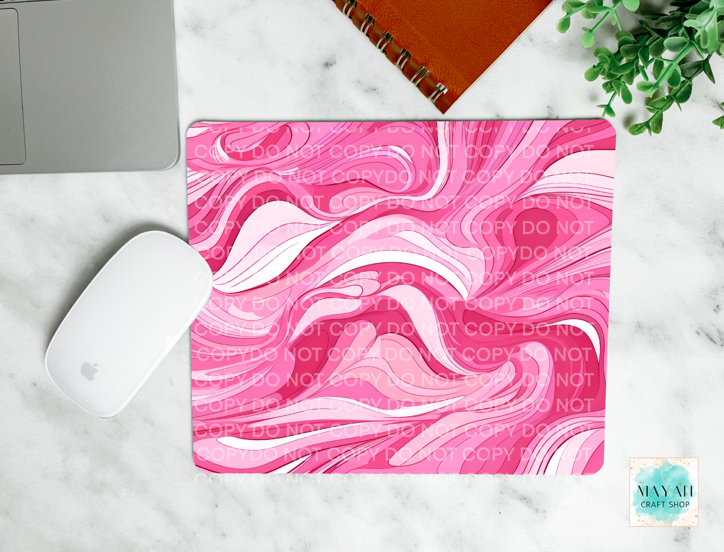 Pink and white marbled mouse pad on a marble surface with a laptop and plant.