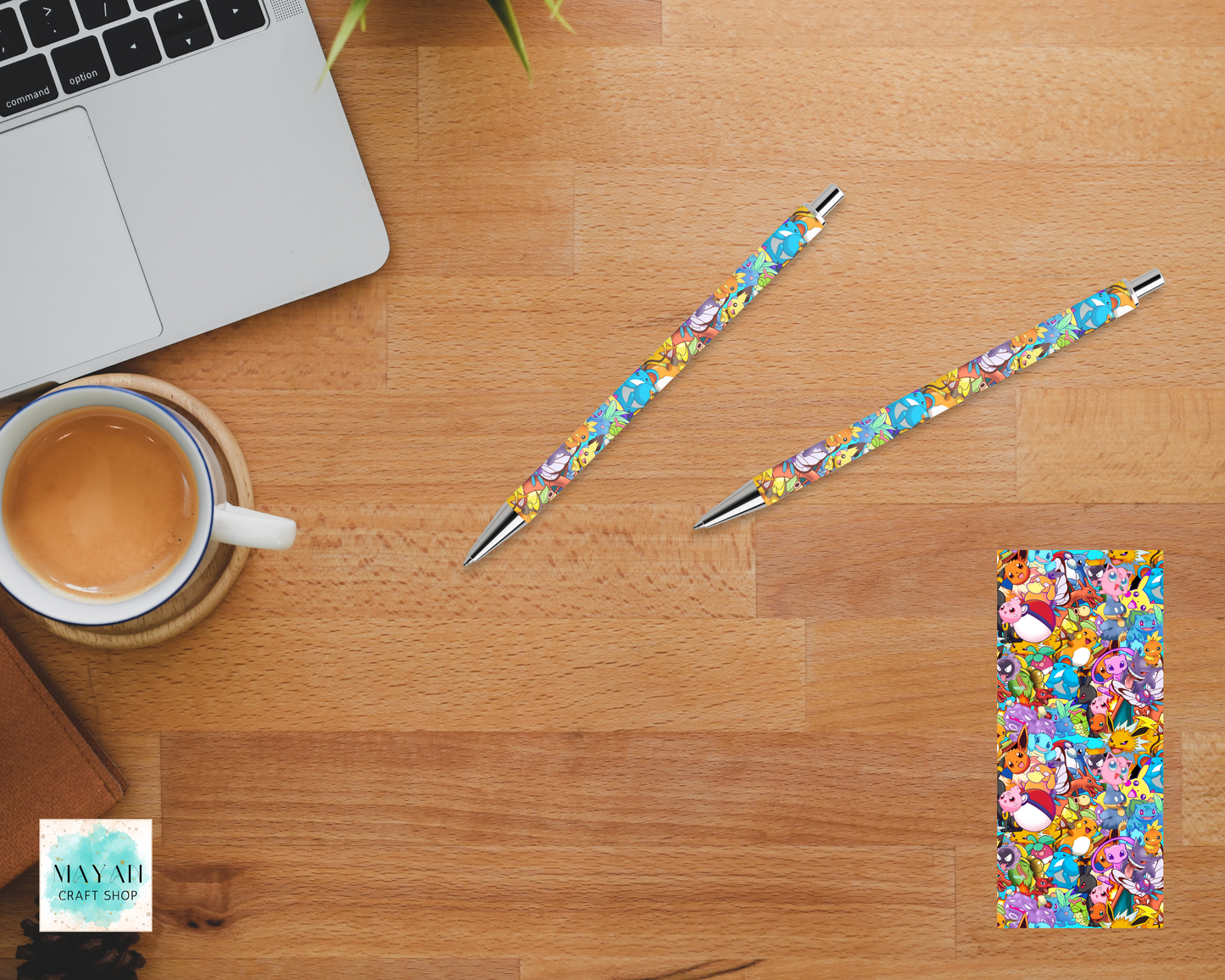 Colorful pens and notebook on a wooden desk with a laptop and coffee cup.