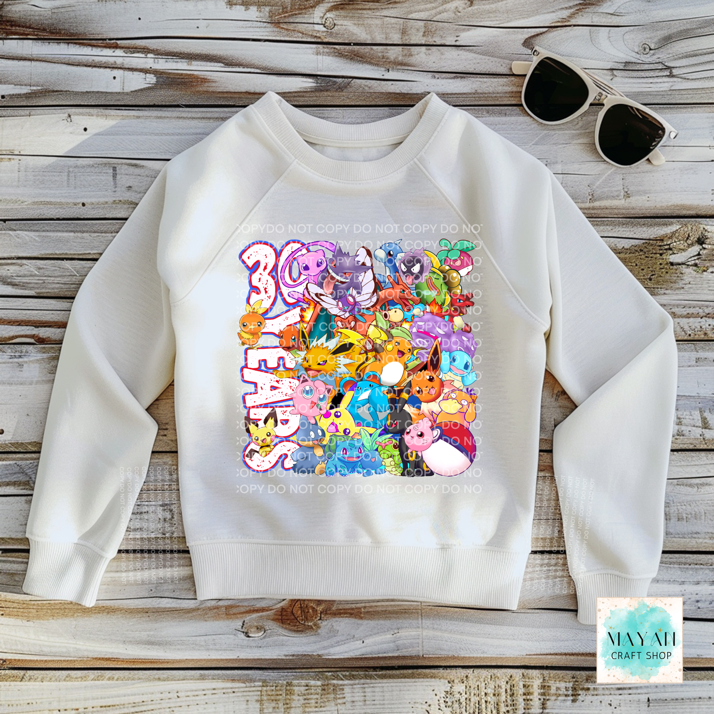 White sweatshirt with colorful graphic design on a wooden surface, accompanied by sunglasses.