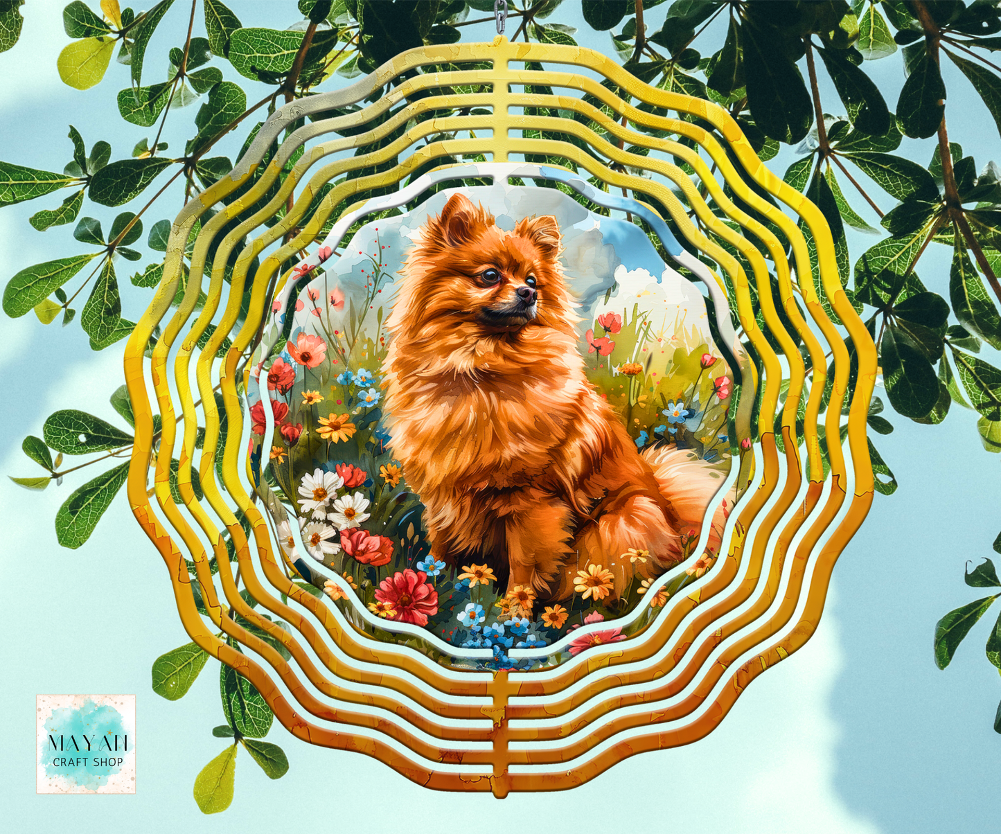 A wind spinner, featuring a printed illustration of a fluffy orange dog in a flower meadow. The piece is displayed against a background of green leaves and a light blue sky.