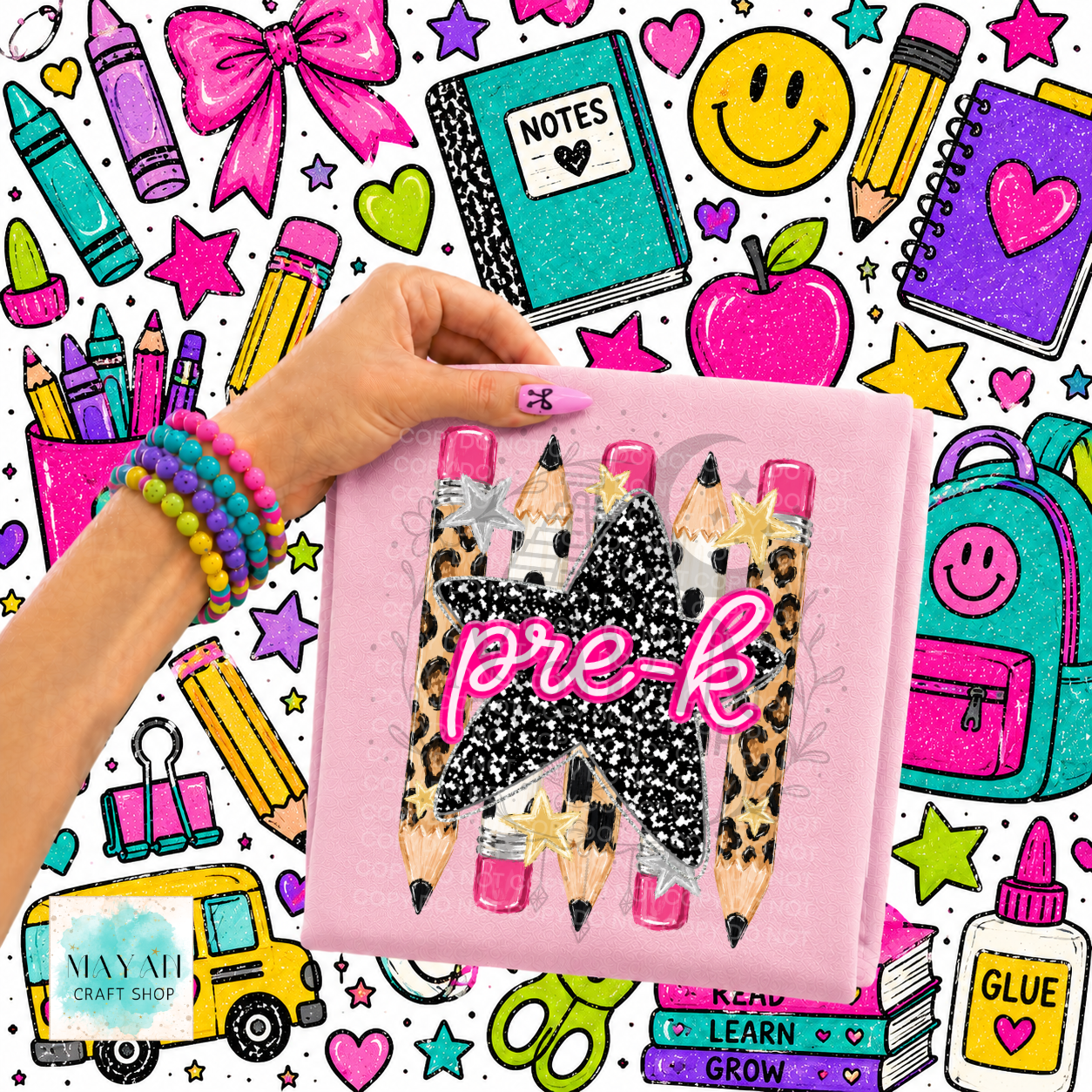 A hand holds a pink shirt featuring three decorative pencils with leopard print, black glitter, and pink glitter tips, with the words 'pre-k' in pink glitter. The background is a busy, colorful school-supplies illustration with crayons, notebooks, an apple, stars, and a yellow bus.