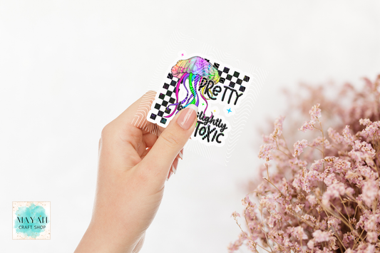 Hand holding a colorful sticker with text, blurred pink flowers in the background