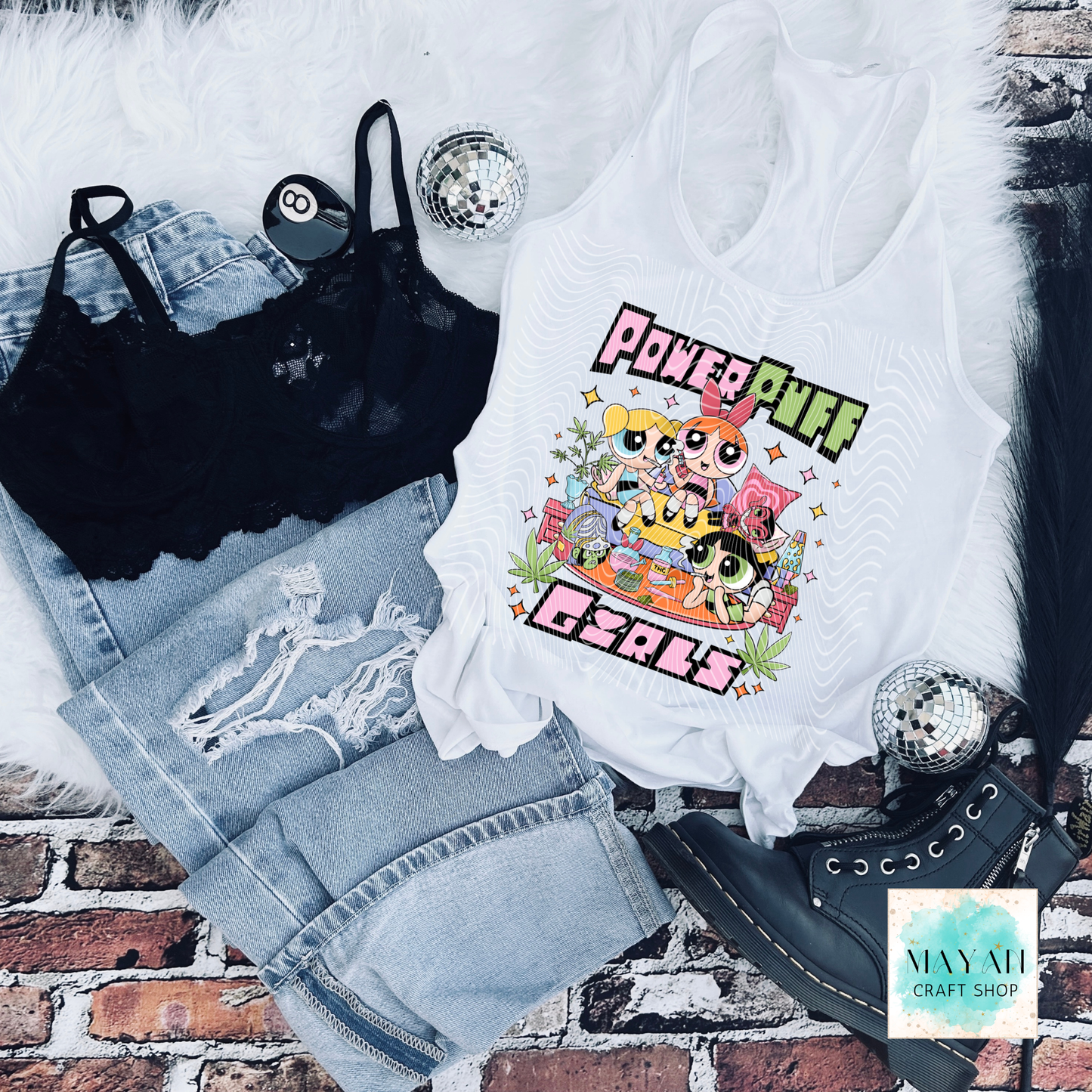 White tank top with vibrant design, black bralette, denim shorts, and black high-heeled shoes on a brick surface.