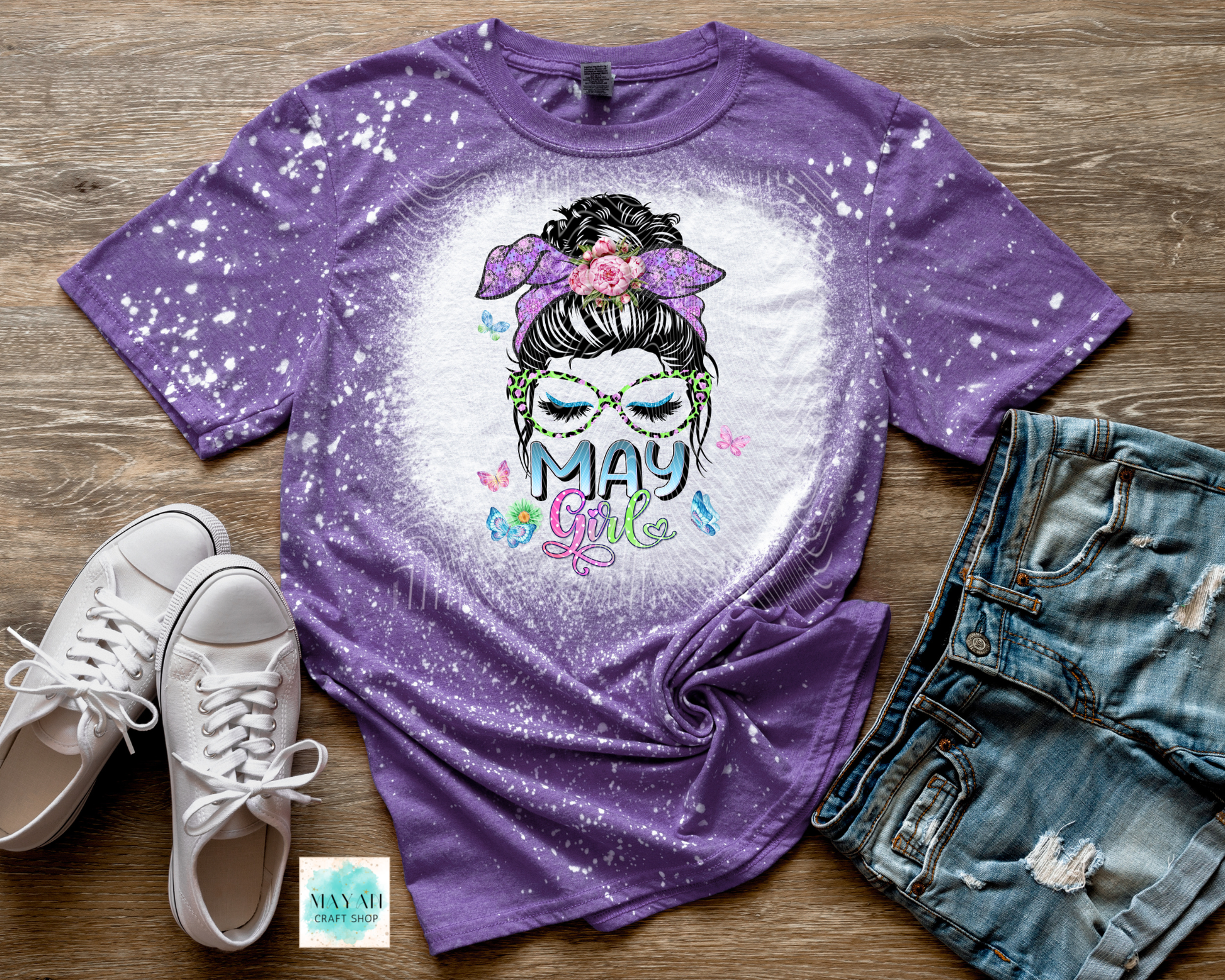 Purple t-shirt with 'May Girl' design on a wooden surface with shoes and jeans.